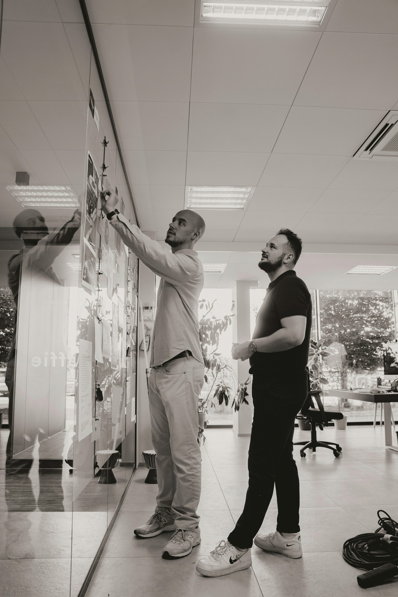 Two colleagues reviewing notes on a glass wall in an office